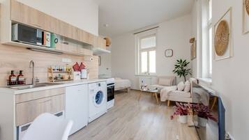 A modern kitchen with a washing machine, a dining area with a table and chairs, and a living area with a sofa.