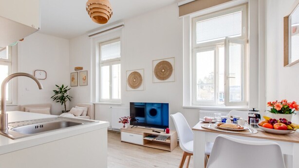 Une cuisine moderne dotée d’un évier intégré, un coin repas avec une table et des chaises, et un téléviseur en arrière-plan.