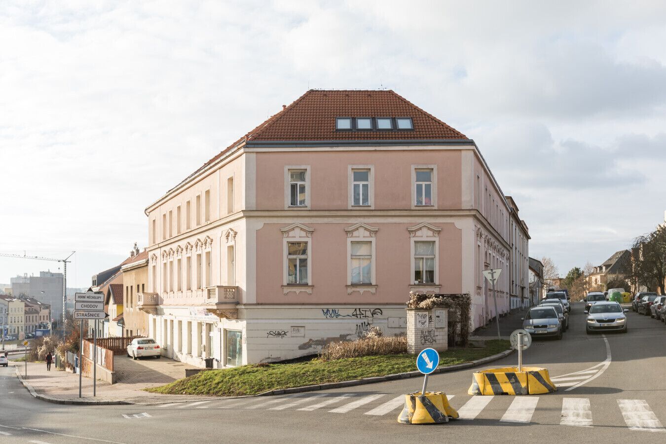A pink building with a tiled roof, a pedestrian crossing, and a blue directional sign.