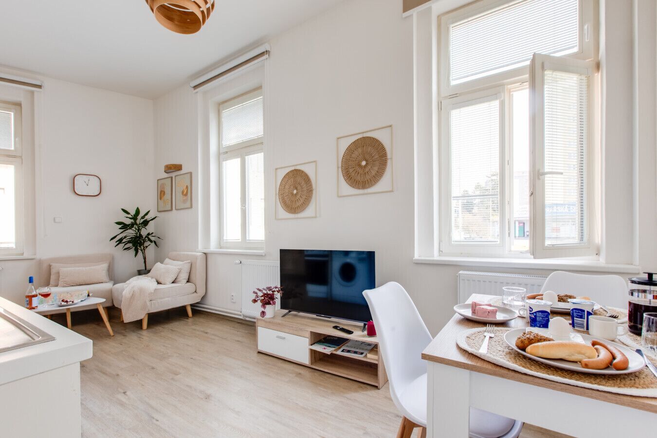 Un salon moderne avec un canapé, un téléviseur, une table à manger où est servi le petit-déjeuner, et de grandes fenêtres.