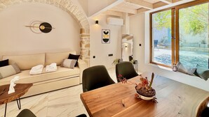 Un interior moderno con un arco de piedra, techo de madera, un sofá, una mesa de comedor y vista a una piscina.