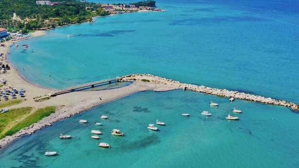 Vista aérea de una zona costera con un muelle, barcos y una playa.