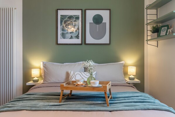 A neatly made bed with a tray of breakfast items, two bedside lamps, and framed artwork on the wall.