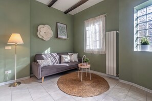 A living room with a sofa, a lamp, a round rug, a small table with a plant, and a window with a view.