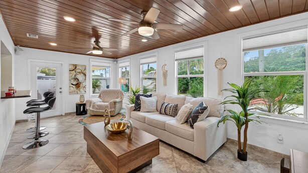 A spacious room with a wooden ceiling, a large window, a sofa, a coffee table, and a bar area with stools. - Tropical Home: Private Pool, Near Clearwater Beach (Clearwater)
