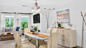 A dining area with a white table, beige chairs, a chandelier, and a painting on the wall. - Tropical Home: Private Pool, Near Clearwater Beach (Clearwater)