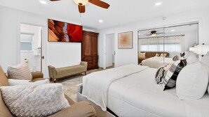 A bedroom with a bed, a bench, a ceiling fan, a large painting, and a mirror. - Tropical Home: Private Pool, Near Clearwater Beach (Clearwater)