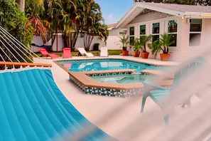 A swimming pool with a tiled deck, lounge chairs, and potted plants.