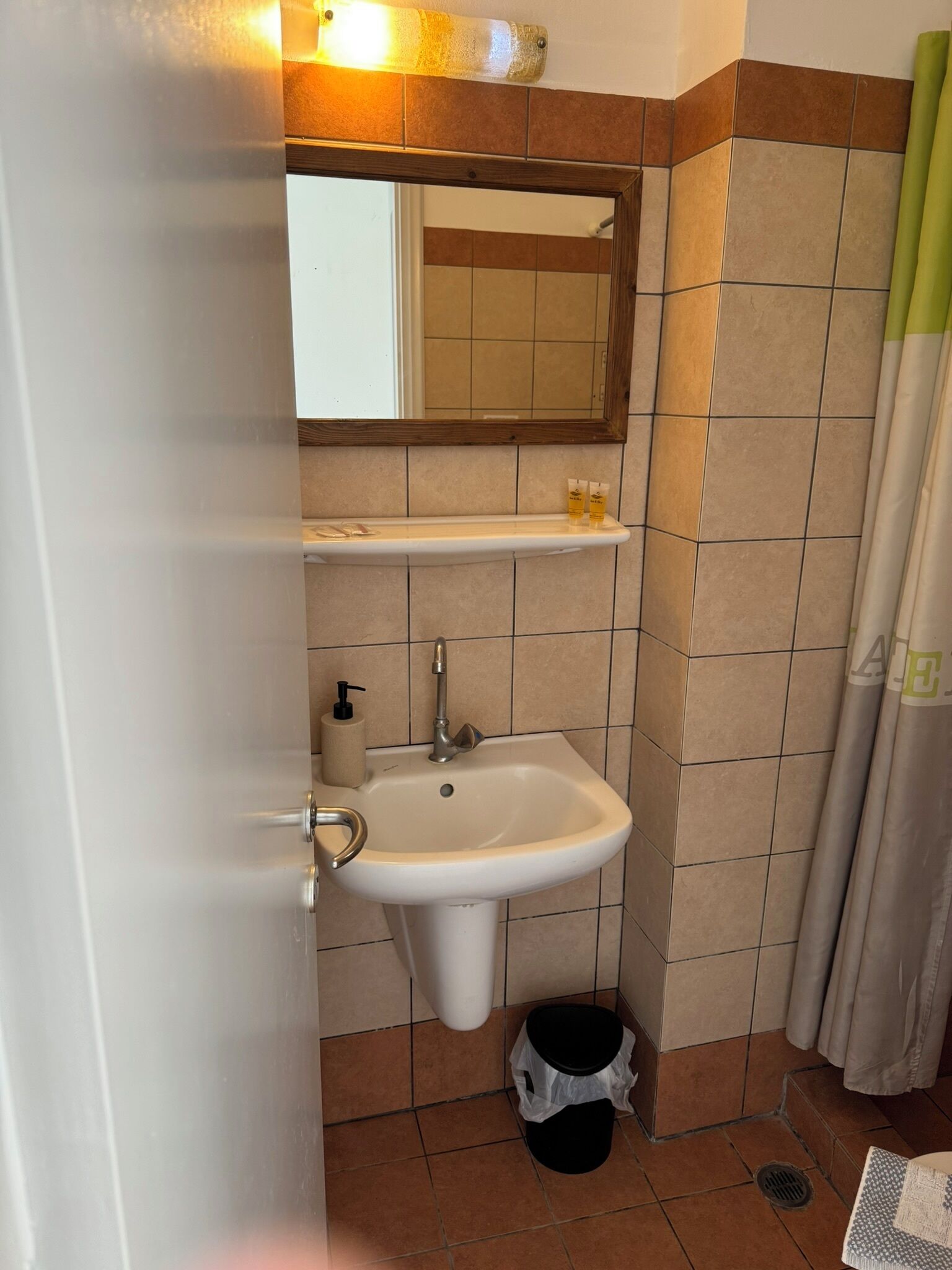 A bathroom with a sink, mirror, and a trash bin.