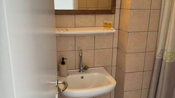 A bathroom with a sink, mirror, and a trash bin.