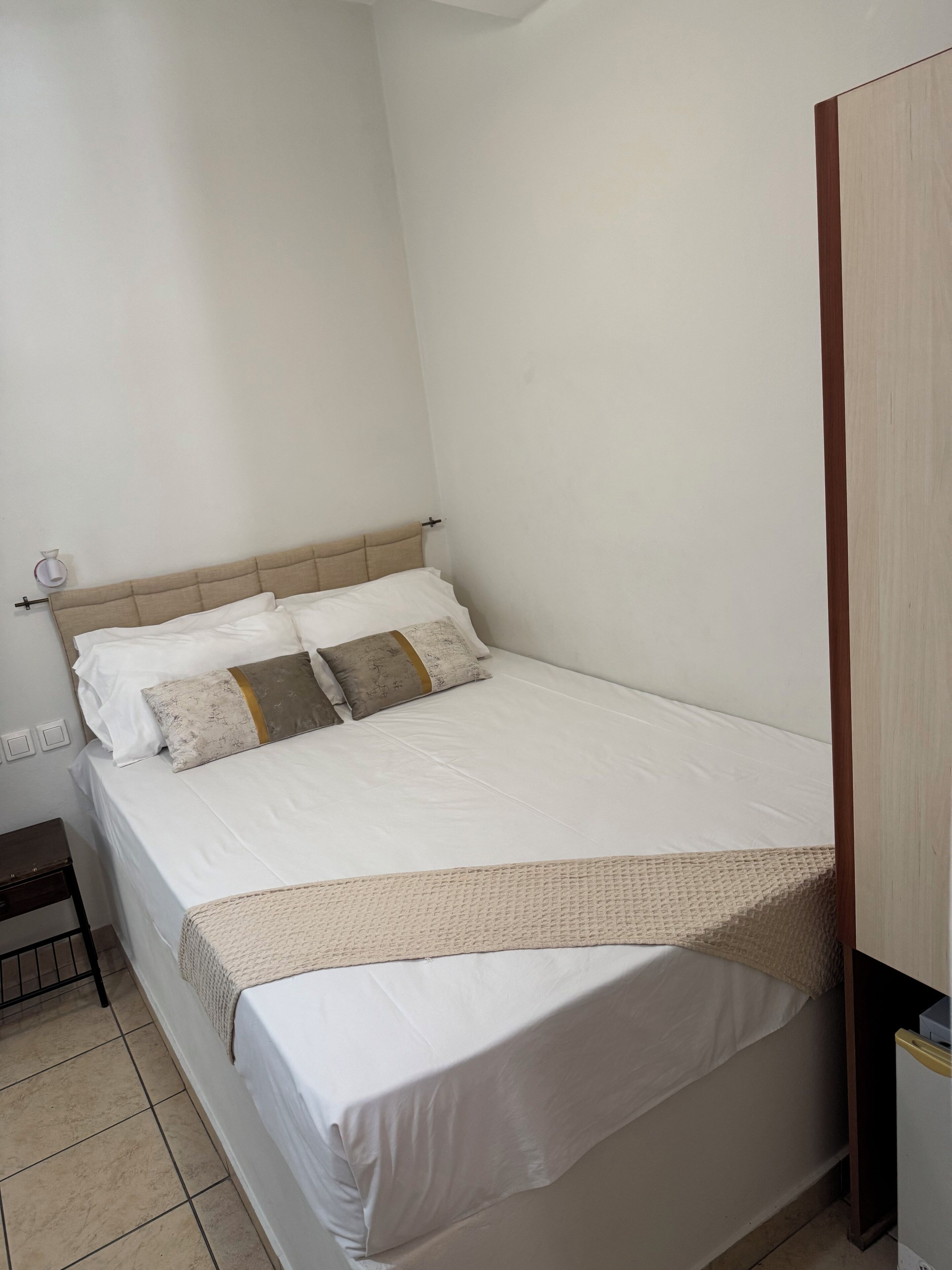 Una cama individual con cabecera, una mesita de noche y una lámpara fijada a la pared.