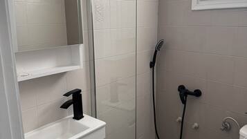 A bathroom with a glass shower enclosure, a white sink, and a toilet.