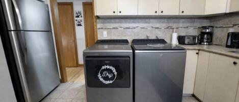 Cocina compacta con electrodomésticos de acero inoxidable, incluyendo un refrigerador y una estufa, y armarios de colores claros.