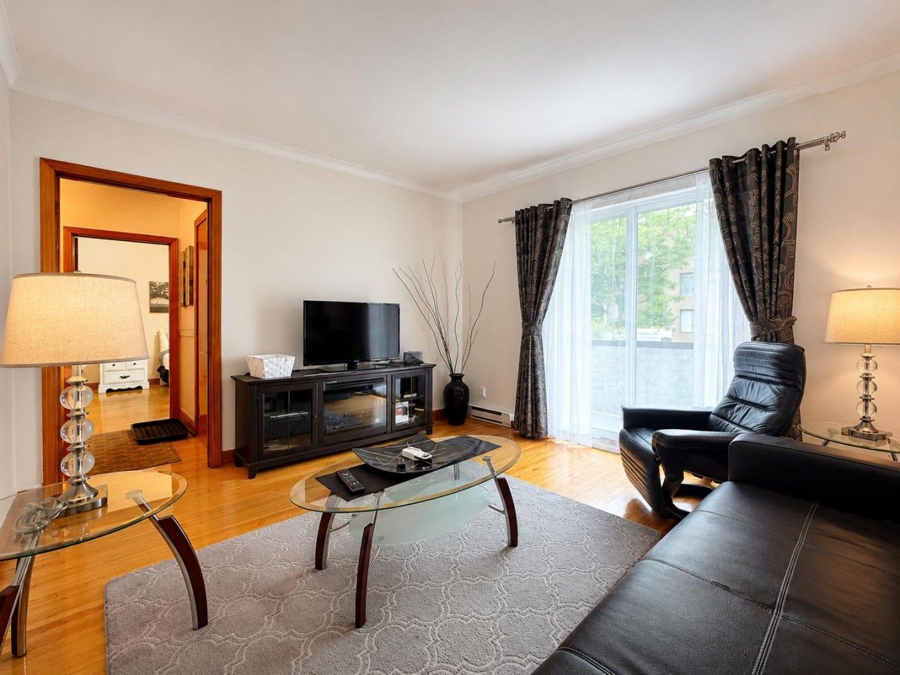 A living room with a glass coffee table, leather sofa, and a television on a black cabinet.