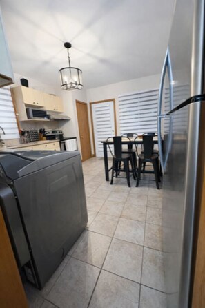 A compact kitchen with a dining area, featuring a refrigerator, stove, and cabinets. - Cozy 3BR Getaway with Backyard & Included parking (Montreal)