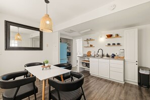 A modern kitchen with white cabinets, a dining table with chairs, and pendant lighting. - NEW! Driftwood Dunes - 3 Private Units - Sleeps 14 (Carolina Beach)