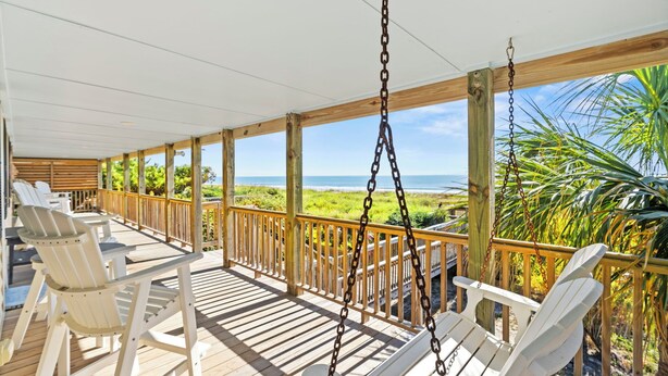 A covered outdoor deck with white Adirondack chairs, a swing, and a view of the ocean. - Mini Golf Heated Pool Ocean Front Family Fun (Holden Beach)