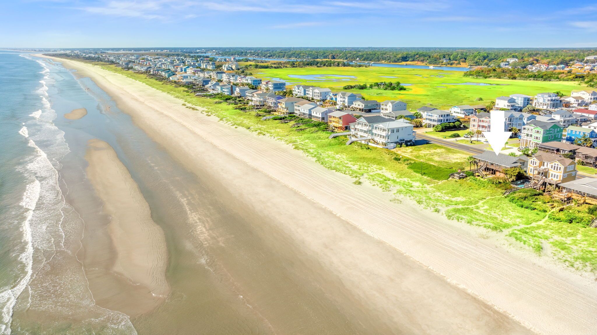 A coastal residential area with beachfront properties, a road, and green fields.