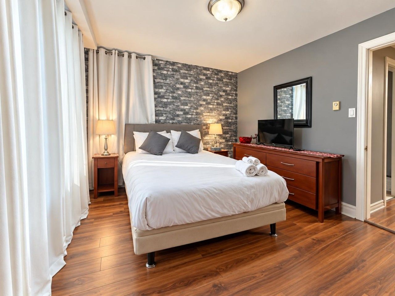A hotel room with a bed, a nightstand, a dresser, a television, and a stone accent wall.