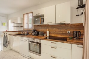 A modern kitchen with white cabinets, a wooden countertop, a built-in oven, and a coffee maker. - Le Petit Coin du Lac – À 10 min du lac à pied (Saint-Pée-sur-Nivelle)