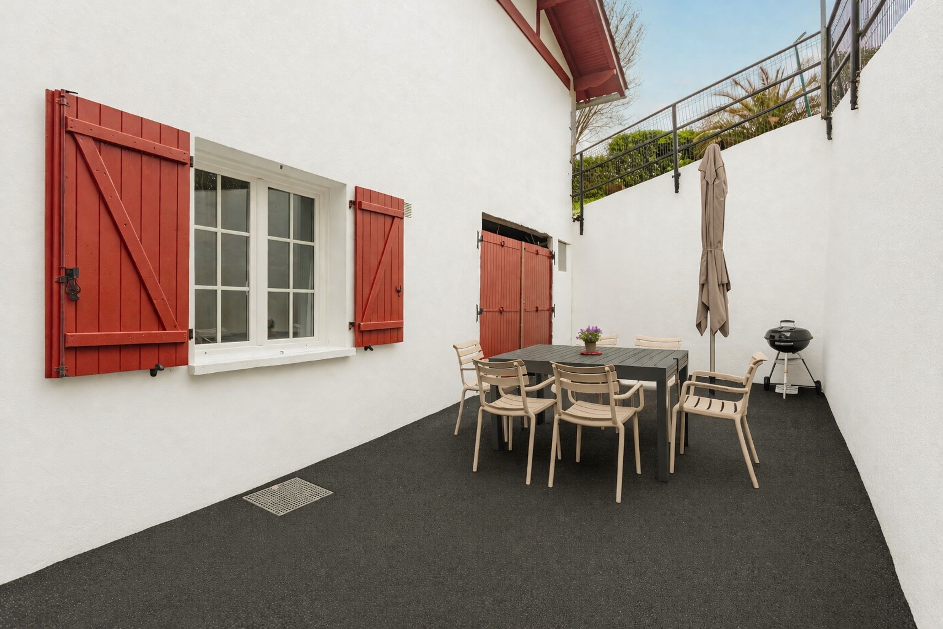 A patio with a table and chairs, a grill, and red shutters on the windows.