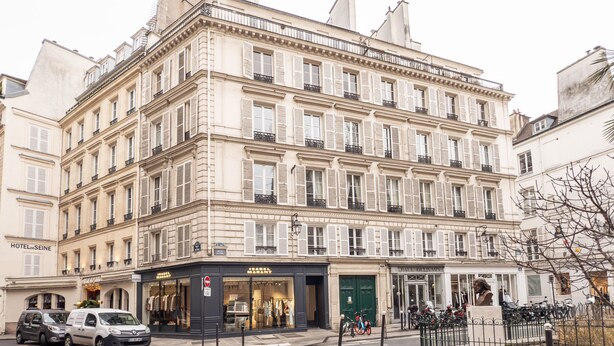 A multi-story building with a classic European architectural style, featuring a ground-floor shop and a green door entrance.