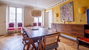 A dining room with a wooden table, red cushioned chairs, a chandelier, and a large painting on the wall.