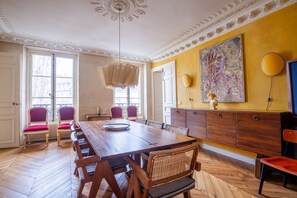 A dining room with a wooden table, red cushioned chairs, a chandelier, and a large painting on the wall. - Saint Germain Artiste (Paris)