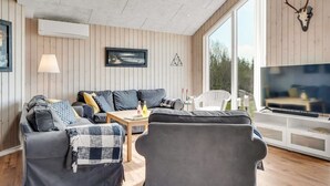 Ein modernes Wohnzimmer mit einer Couch, Sesseln, einem Fernseher und einem großen Fenster.