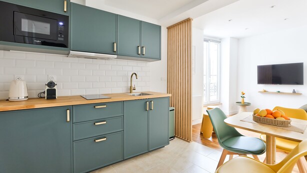 Een moderne keuken met turquoise kastjes, een magnetron en een spoelbak. Er is een zithoek met een tafel en stoelen, en een televisie aan de muur bevestigd.