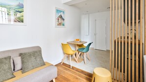 Een moderne woonkamer met een bank, een eettafel met stoelen, houten vloeren en uitzicht op de omgeving.