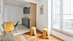 Een moderne keuken met houten kastjes, een eethoek met een gele tafel en stoelen, en een groot raam met uitzicht op de straat.