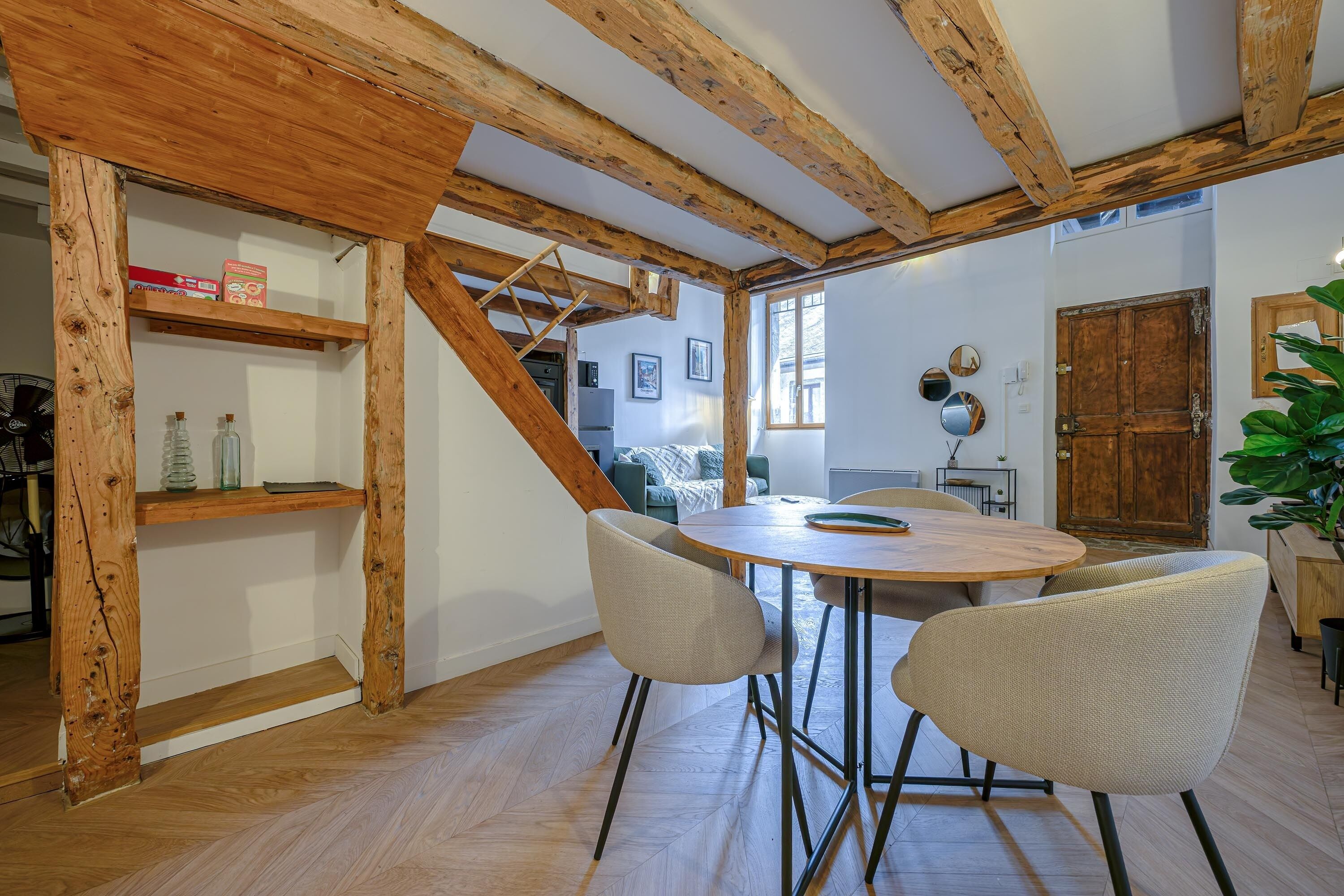 Une pièce avec un plafond en bois, une table ronde entourée de chaises, un escalier et une porte.
