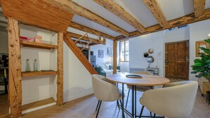 Una habitación con techo de madera, una mesa redonda con sillas, una escalera y una puerta.
