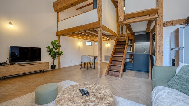 Una sala de estar moderna con televisor, asientos, una escalera y una zona de cocina.