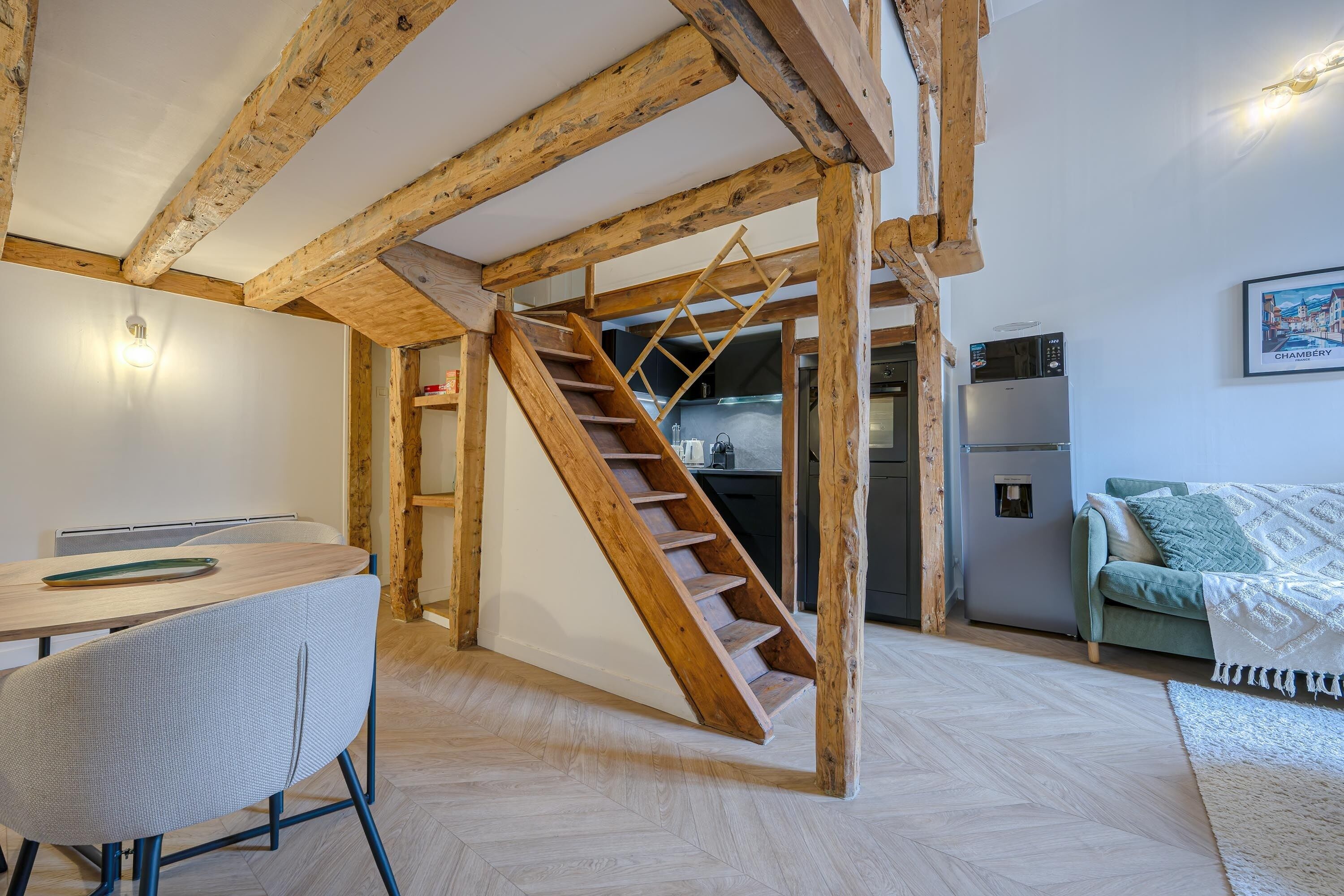 Une pièce comprenant un escalier en bois, un coin repas avec une table et des chaises, et un espace cuisine équipé d’appareils électroménagers.