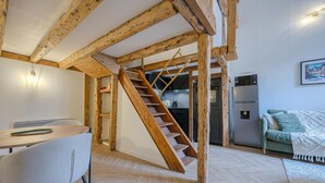 Una habitación con escalera de madera, zona de comedor con mesa y sillas, y área de cocina con electrodomésticos.