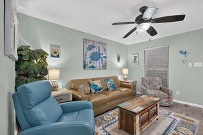 A living room with a ceiling fan, a blue armchair, a brown sofa, and a patterned rug. - Beachside  condo in gorgeous Gulf Shores-Very close to Beach (Gulf Shores)