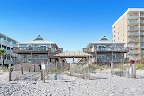 Ein Strandhotel mit mehreren Balkonen, einem überdachten Gang und einem Sandstrand.