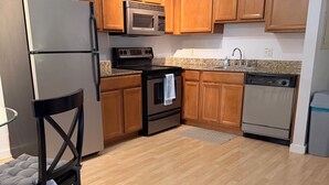 Una cocina con armarios de madera, un refrigerador de acero inoxidable, un microondas, un horno, un lavavajillas y una silla con una etiqueta.