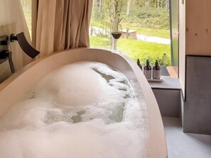 A bathtub filled with bubbles, a window with curtains, and a view of greenery outside. - 2 bedroom accommodation in Chipping Norton (Chipping Norton)