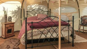 Una cama con una colcha estampada, una mesita de noche de madera con un jarrón y un farol, y una silla con cojín.