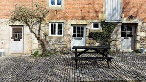 A stone building with a brick facade, a wooden door labeled 'WISELS,' a small window, and a picnic table on a cobblestone ground. - 2 bedroom accommodation in Carsington, near Ashbourne (Carsington, near Ashbourne)