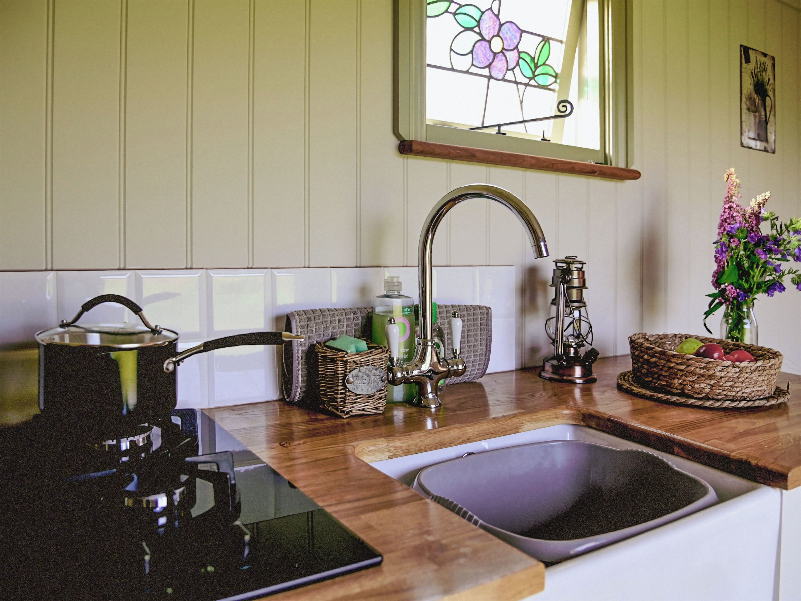 Una cocina con un lavamanos, un hervidor, una cesta y un florero con flores.