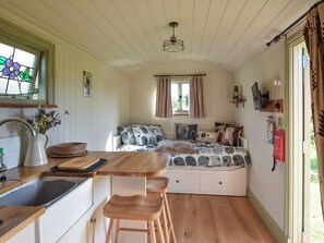 Een compacte, knusse kamer met een kitchenette, een bed met een geborreld kleed en een raam met gordijnen.