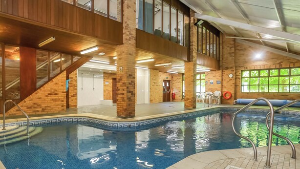 An indoor swimming pool with a tiled edge, a metal handrail, and a brick wall. - Spacious stone barn close to Matlock and Carsington Water. (Carsington, near Ashbourne)