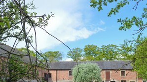 A brick building with multiple windows and doors, a gravel courtyard, and a wooden gate. - Spacious stone barn close to Matlock and Carsington Water. (Carsington, near Ashbourne)