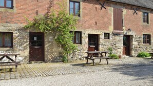 A traditional brick building with stone walls, wooden doors, and a gravel courtyard. - Spacious stone barn close to Matlock and Carsington Water. (Carsington, near Ashbourne)