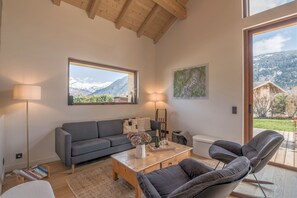 A living room with a sofa, armchairs, a coffee table, and a view of mountains.