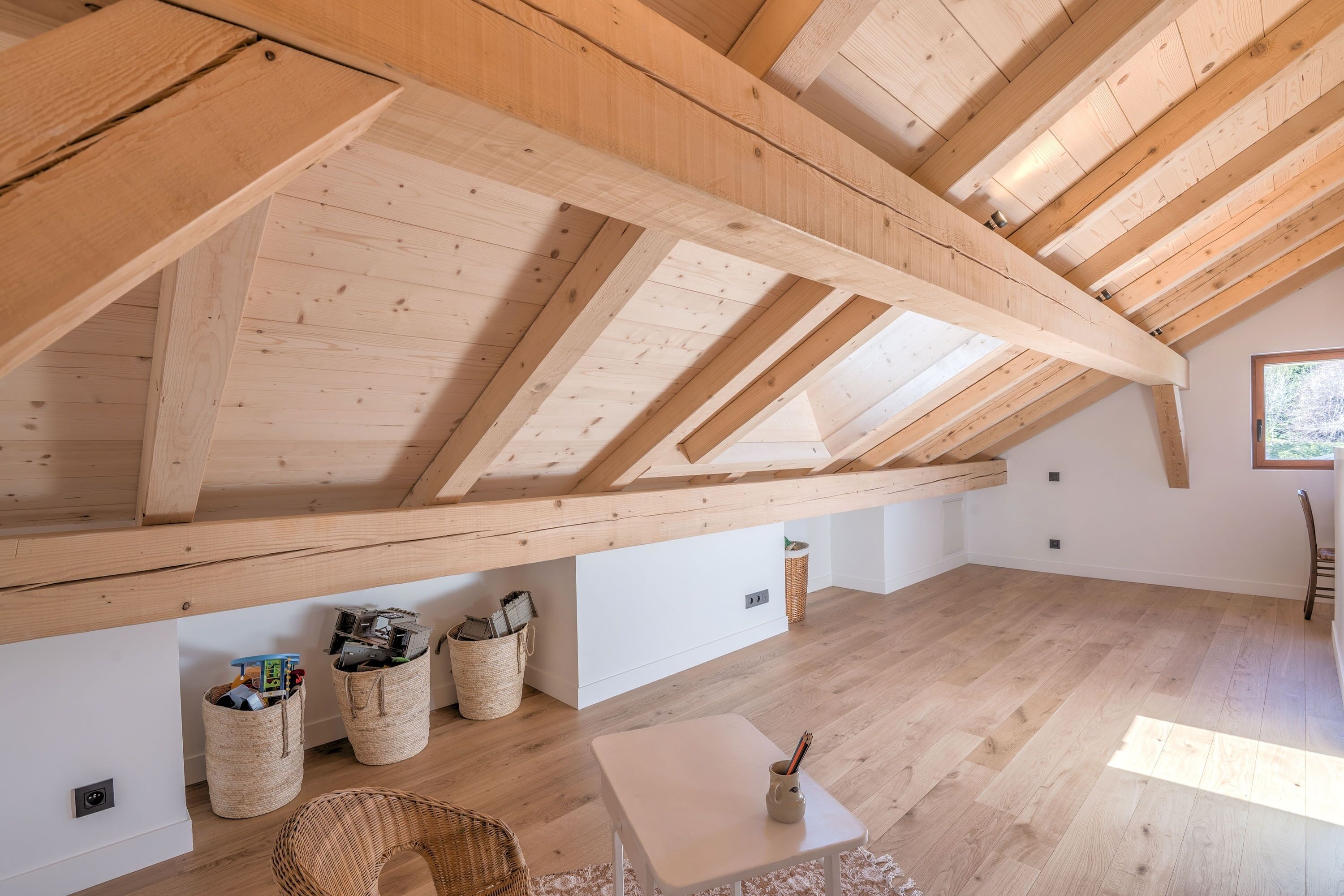 Una habitación con vigas de madera, una mesa blanca, cestas de mimbre y una silla.